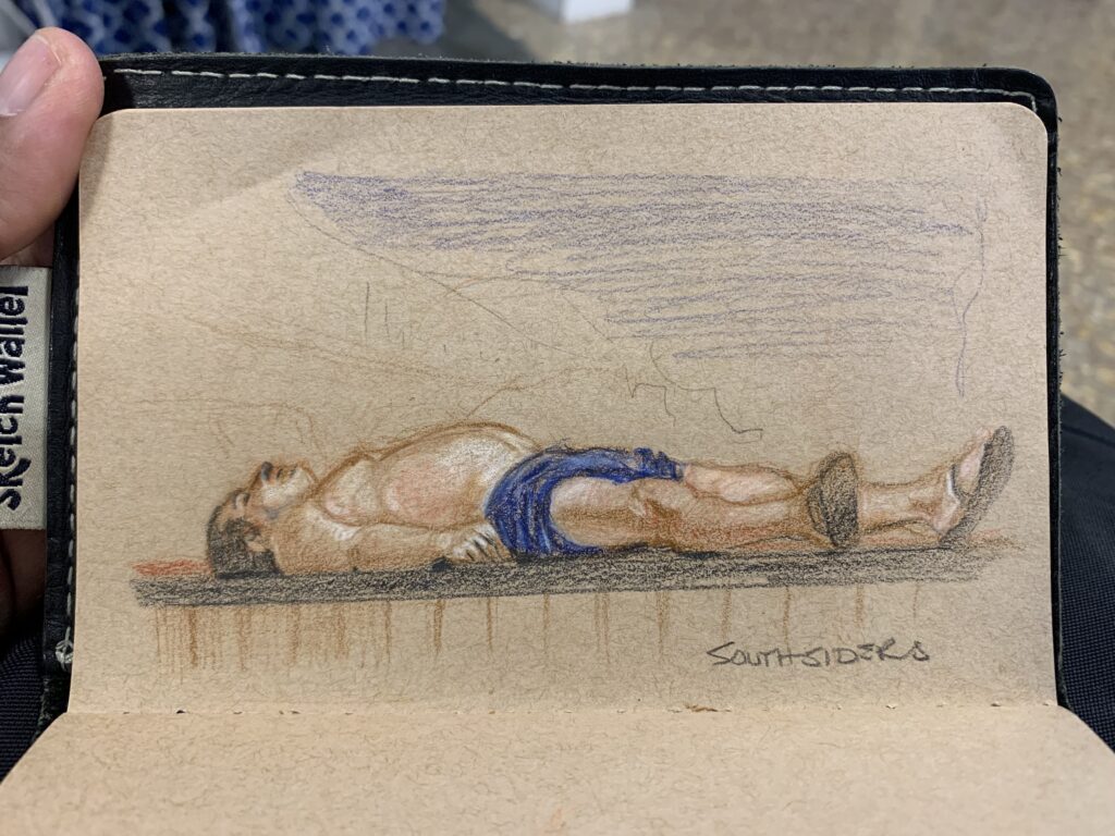 Colour pencil sketch of a European man sunbaking, lying down on his back, wearing blue shorts.Southsiders Bistro, Marsaskala, Malta 2022 By Maria Pena, Artist and Illustrator. Also known as Maria de Los Angeles Pena. #Storyboarderau #storyboarder